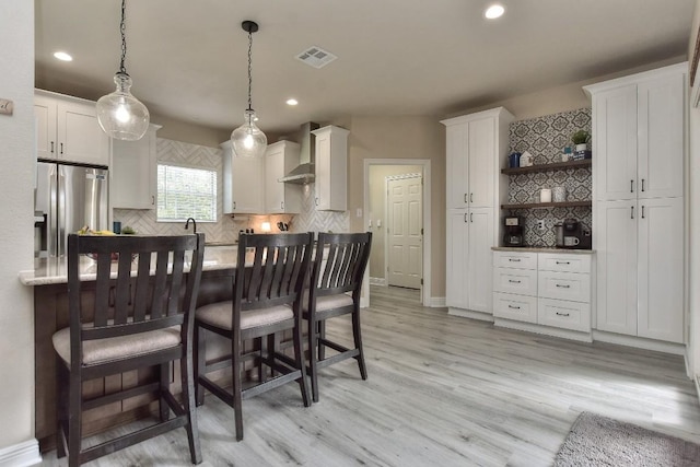 kitchen featuring visible vents, stainless steel refrigerator with ice dispenser, open shelves, white cabinets, and wall chimney range hood