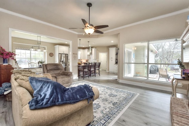 living room with light wood-type flooring, baseboards, ornamental molding, and a ceiling fan