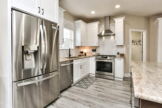 kitchen with a sink, wall chimney range hood, white cabinetry, stainless steel appliances, and light wood finished floors