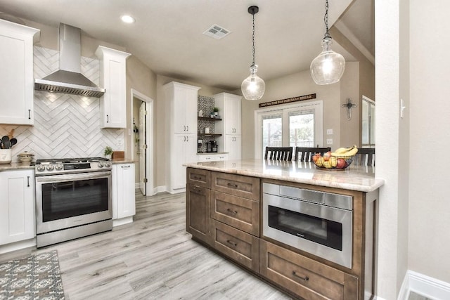 kitchen featuring tasteful backsplash, light wood finished floors, wall chimney range hood, white cabinets, and stainless steel appliances