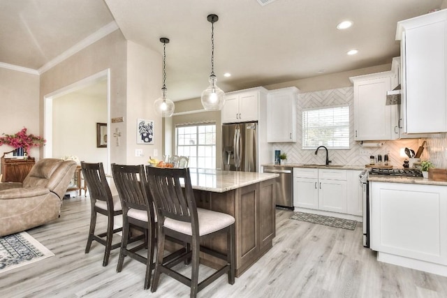 kitchen with a sink, backsplash, white cabinetry, stainless steel appliances, and a breakfast bar area