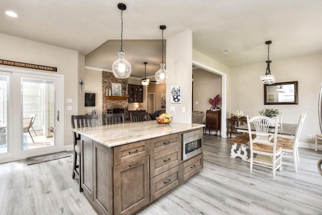 kitchen featuring pendant lighting, stainless steel microwave, light wood-style floors, baseboards, and vaulted ceiling