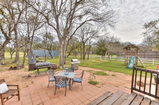 view of patio / terrace with a playground, fence, an outdoor structure, outdoor dining space, and a grill