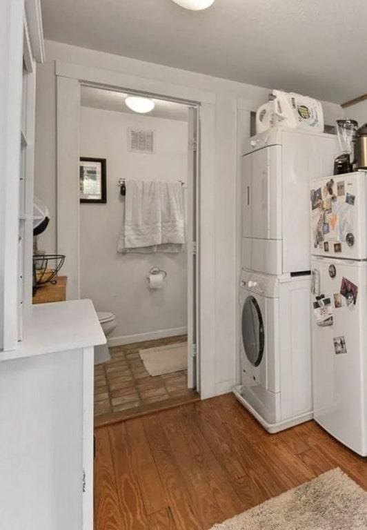 bathroom featuring visible vents, toilet, wood finished floors, and stacked washer / dryer