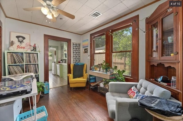 living area with a ceiling fan, crown molding, wood finished floors, and visible vents