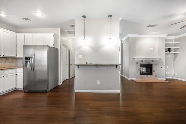 kitchen with light stone countertops, visible vents, dark wood finished floors, stainless steel fridge with ice dispenser, and white cabinets