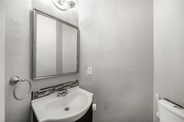 half bathroom with decorative backsplash, toilet, vanity, and a textured wall