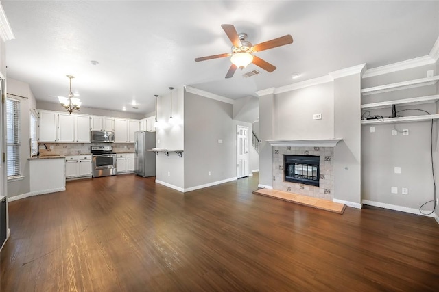 unfurnished living room with visible vents, a sink, dark wood finished floors, a fireplace, and baseboards