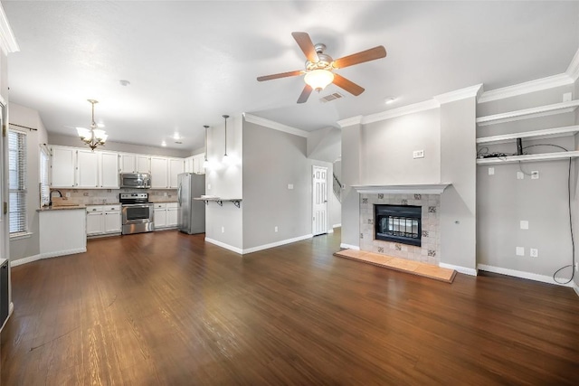 16901 W Stockton Dr, Leander, TX 78641 - unfurnished living room with ceiling fan, crown molding, dark wood-style flooring, a tile fireplace, and a chandelier