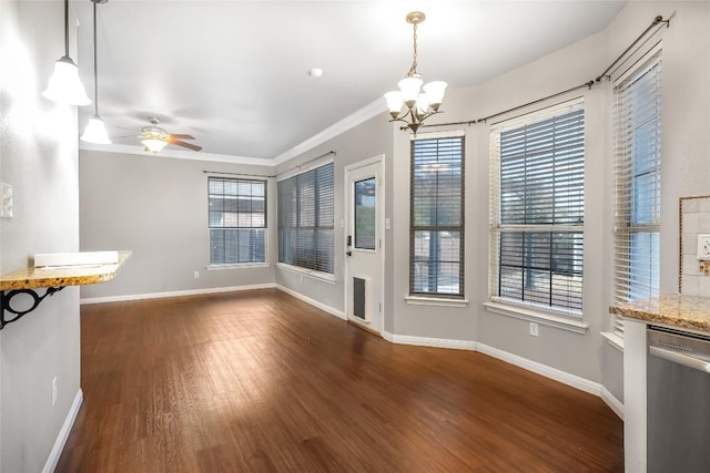 unfurnished dining area featuring baseboards, dark wood-type flooring, ornamental molding, and ceiling fan with notable chandelier