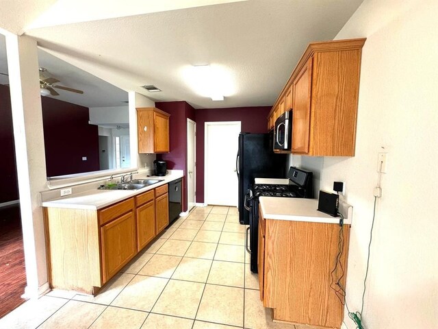 kitchen featuring light tile patterned floors, brown cabinetry, a sink, black appliances, and light countertops