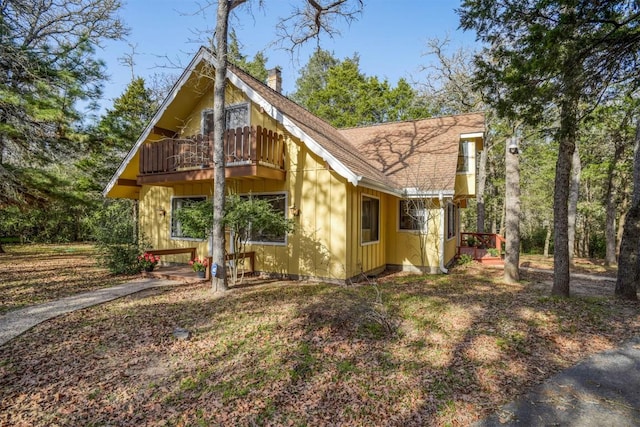 exterior space with board and batten siding, a chimney, a balcony, and roof with shingles