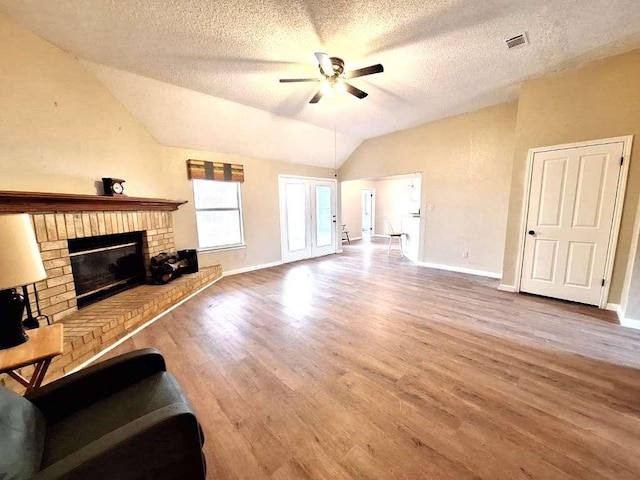 unfurnished living room with a ceiling fan, wood finished floors, visible vents, lofted ceiling, and a brick fireplace