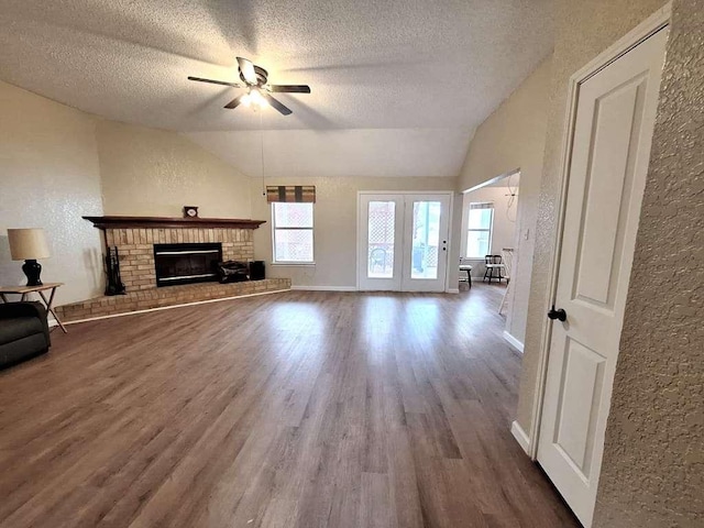 unfurnished living room featuring a brick fireplace, wood finished floors, lofted ceiling, and a textured wall