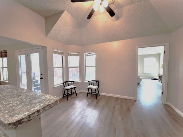 sitting room featuring vaulted ceiling, light wood-style floors, baseboards, and a textured ceiling