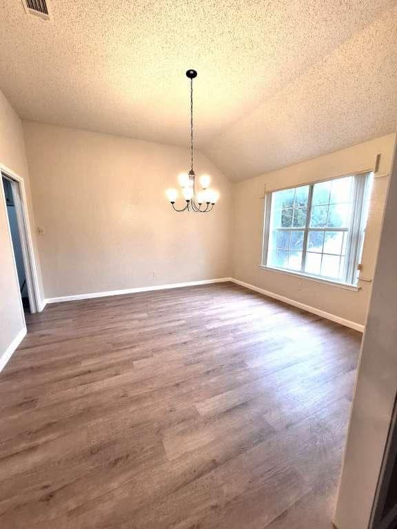 empty room featuring a chandelier, dark wood finished floors, baseboards, and vaulted ceiling