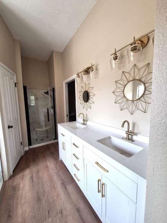 bathroom with a sink, a textured ceiling, wood finished floors, and a shower stall