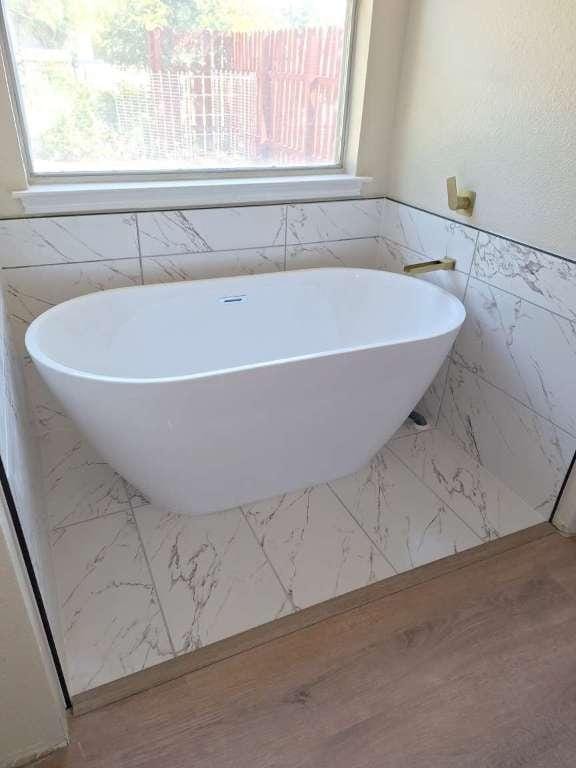 full bath with plenty of natural light, a wainscoted wall, marble finish floor, and a freestanding bath