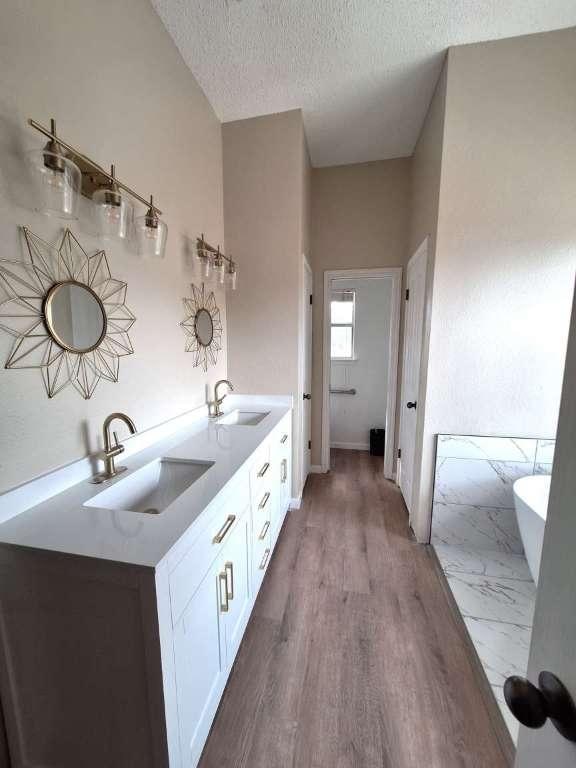 full bathroom with a textured ceiling, double vanity, a freestanding tub, and a sink