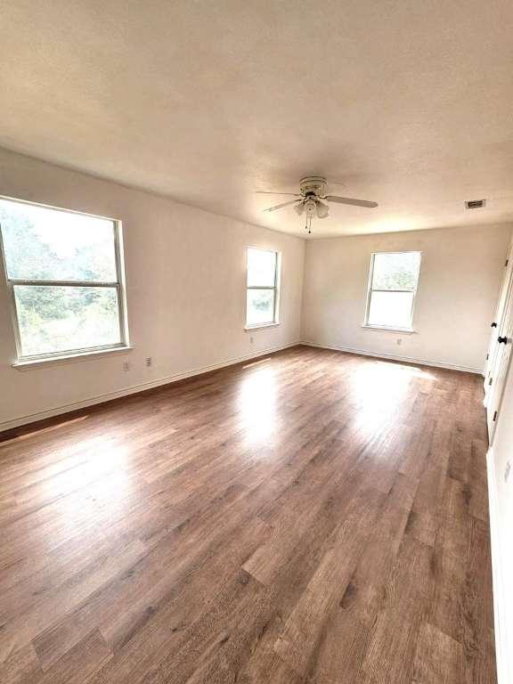 unfurnished room featuring visible vents, a textured ceiling, wood finished floors, baseboards, and ceiling fan