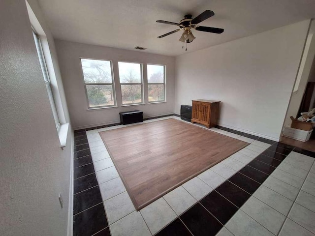 unfurnished living room with tile patterned flooring, visible vents, baseboards, and a ceiling fan