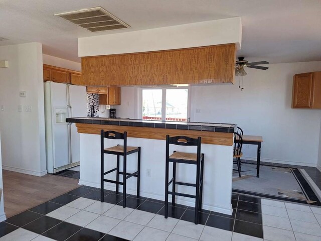 107 Patricia Rd, Georgetown, TX 78628 - kitchen with white fridge with ice dispenser, tile countertops, a breakfast bar area, brown cabinetry, and tile patterned floors
