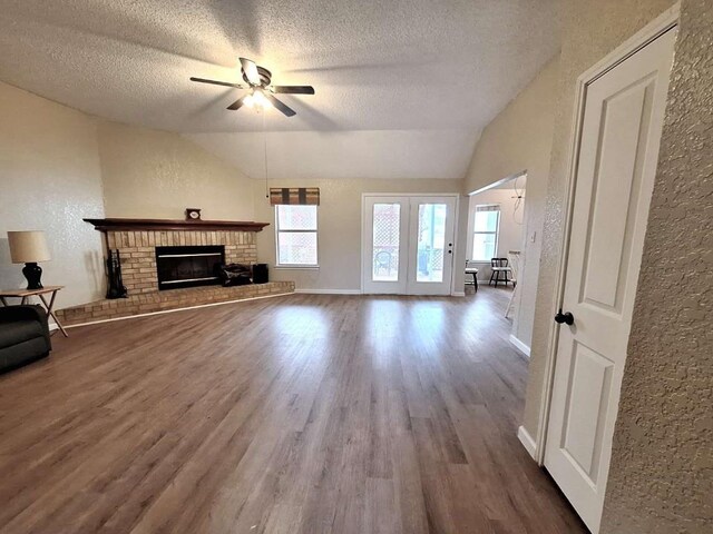 107 Patricia Rd, Georgetown, TX 78628 - unfurnished living room with a textured ceiling, wood finished floors, ceiling fan, a brick fireplace, and vaulted ceiling