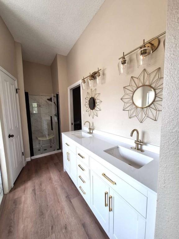 107 Patricia Rd, Georgetown, TX 78628 - bathroom with a shower stall, wood finished floors, a textured ceiling, and double vanity