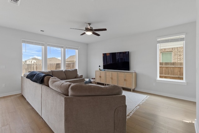 living area featuring visible vents, light wood-style flooring, a ceiling fan, and baseboards