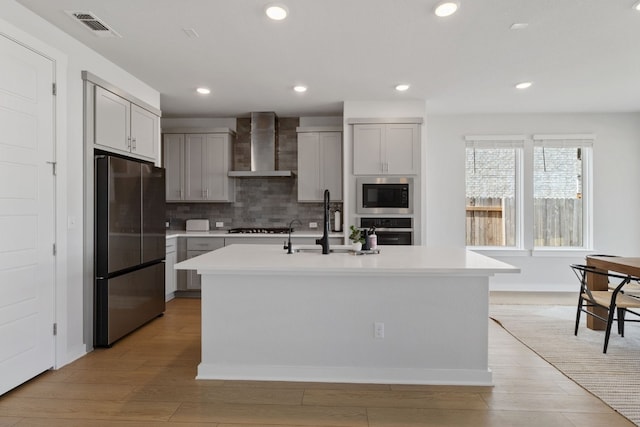 kitchen with visible vents, a sink, light countertops, appliances with stainless steel finishes, and wall chimney exhaust hood