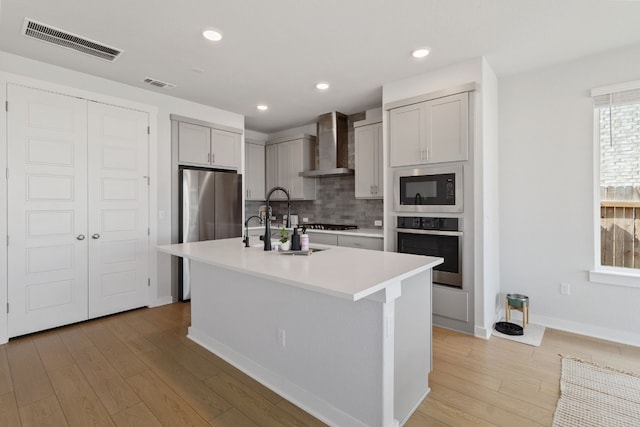 kitchen featuring stainless steel appliances, light wood-style floors, visible vents, and wall chimney range hood