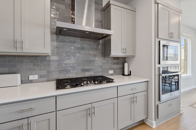 kitchen with decorative backsplash, light countertops, wall chimney range hood, and appliances with stainless steel finishes