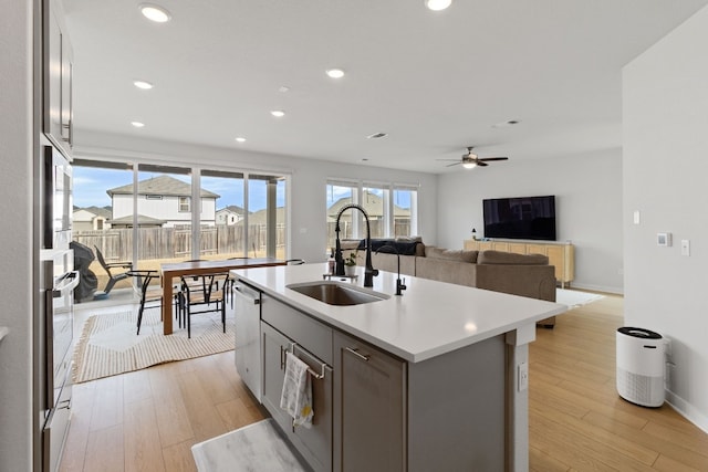 kitchen featuring stainless steel dishwasher, light countertops, light wood-type flooring, and a sink