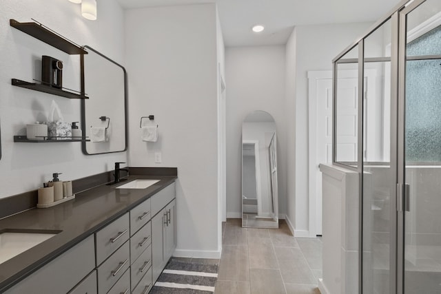 full bath featuring tile patterned flooring, a shower stall, baseboards, double vanity, and a sink