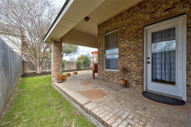 view of exterior entry with a patio, brick siding, a lawn, and fence