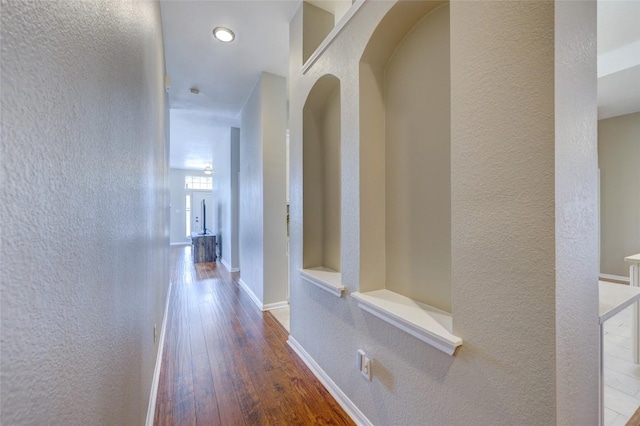 hallway with arched walkways, baseboards, a textured wall, and wood-type flooring