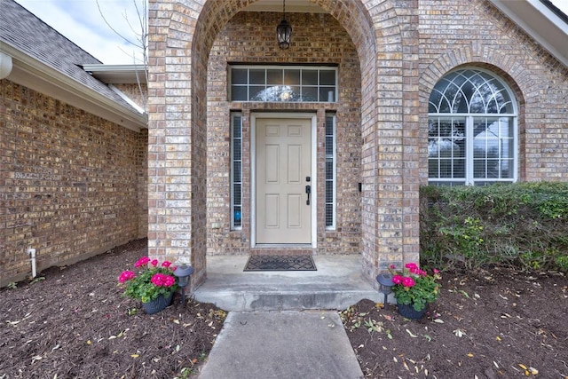 doorway to property with brick siding and a shingled roof