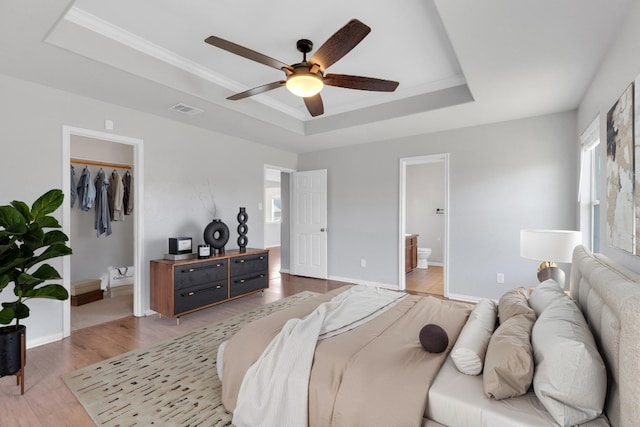 bedroom with visible vents, a walk in closet, a raised ceiling, and light wood-style floors