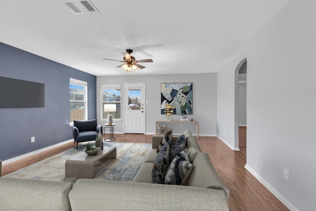 living area with visible vents, baseboards, wood finished floors, arched walkways, and a ceiling fan