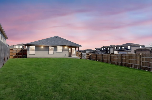 rear view of property featuring a lawn, roof with shingles, and a fenced backyard