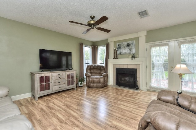 living area featuring ceiling fan, visible vents, light wood-type flooring, and a textured ceiling