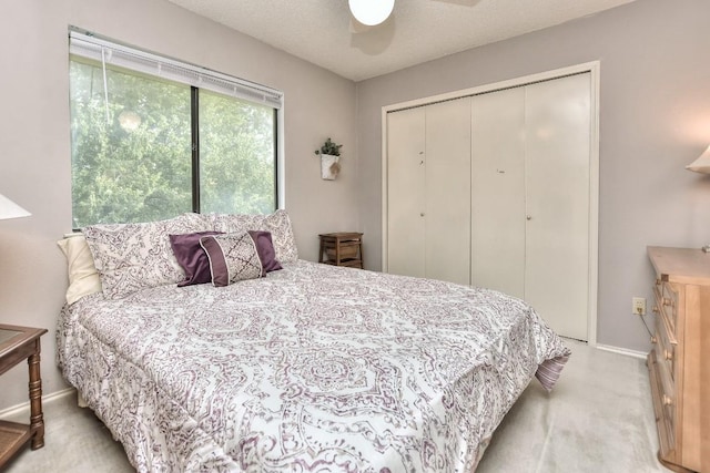 bedroom featuring baseboards, ceiling fan, light carpet, a closet, and a textured ceiling