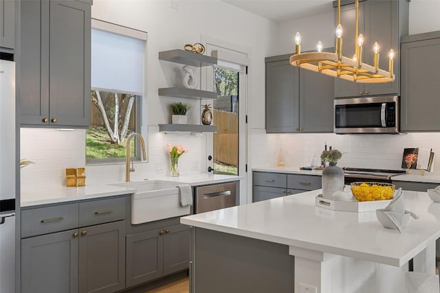 kitchen featuring open shelves, plenty of natural light, gray cabinets, a sink, and stainless steel appliances