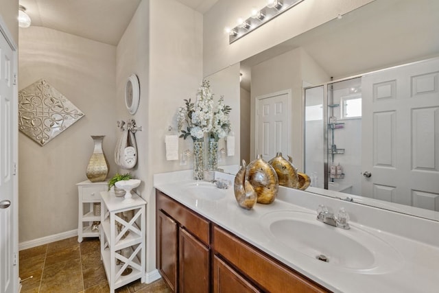 full bath featuring a shower stall, double vanity, baseboards, and a sink