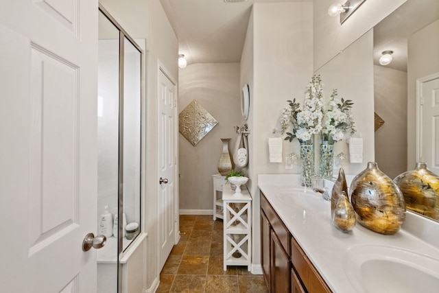 full bathroom with double vanity, a stall shower, baseboards, and a sink