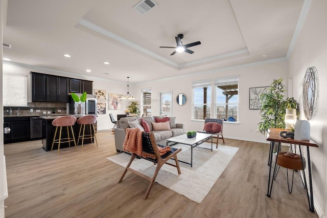 living area with a raised ceiling, light wood-style flooring, crown molding, and visible vents