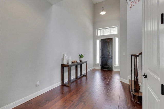 entrance foyer featuring a healthy amount of sunlight, dark wood-style flooring, a towering ceiling, and baseboards