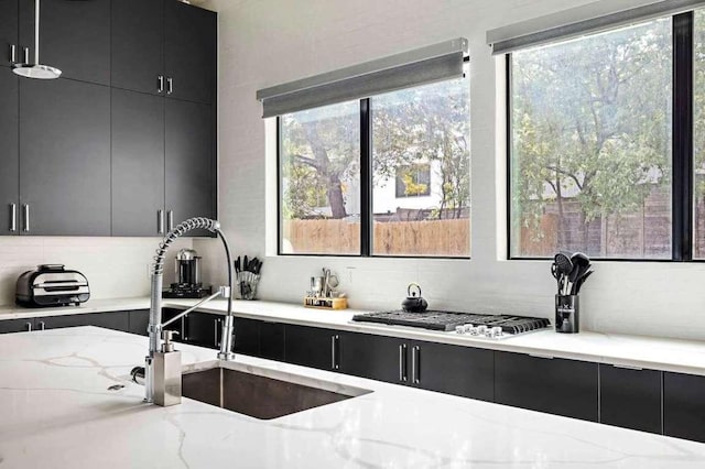 kitchen featuring a sink, plenty of natural light, backsplash, and dark cabinetry