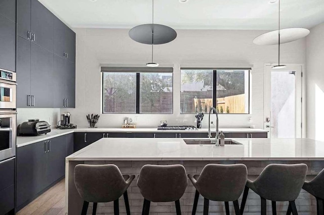 kitchen with a sink, stainless steel oven, a kitchen breakfast bar, modern cabinets, and light wood-type flooring