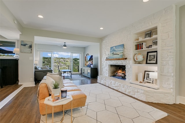 living room with a stone fireplace, built in shelves, wood finished floors, and baseboards